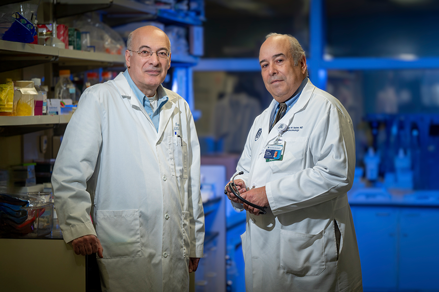 Two male scientists stand in a lab. Both are wearing lab coats.