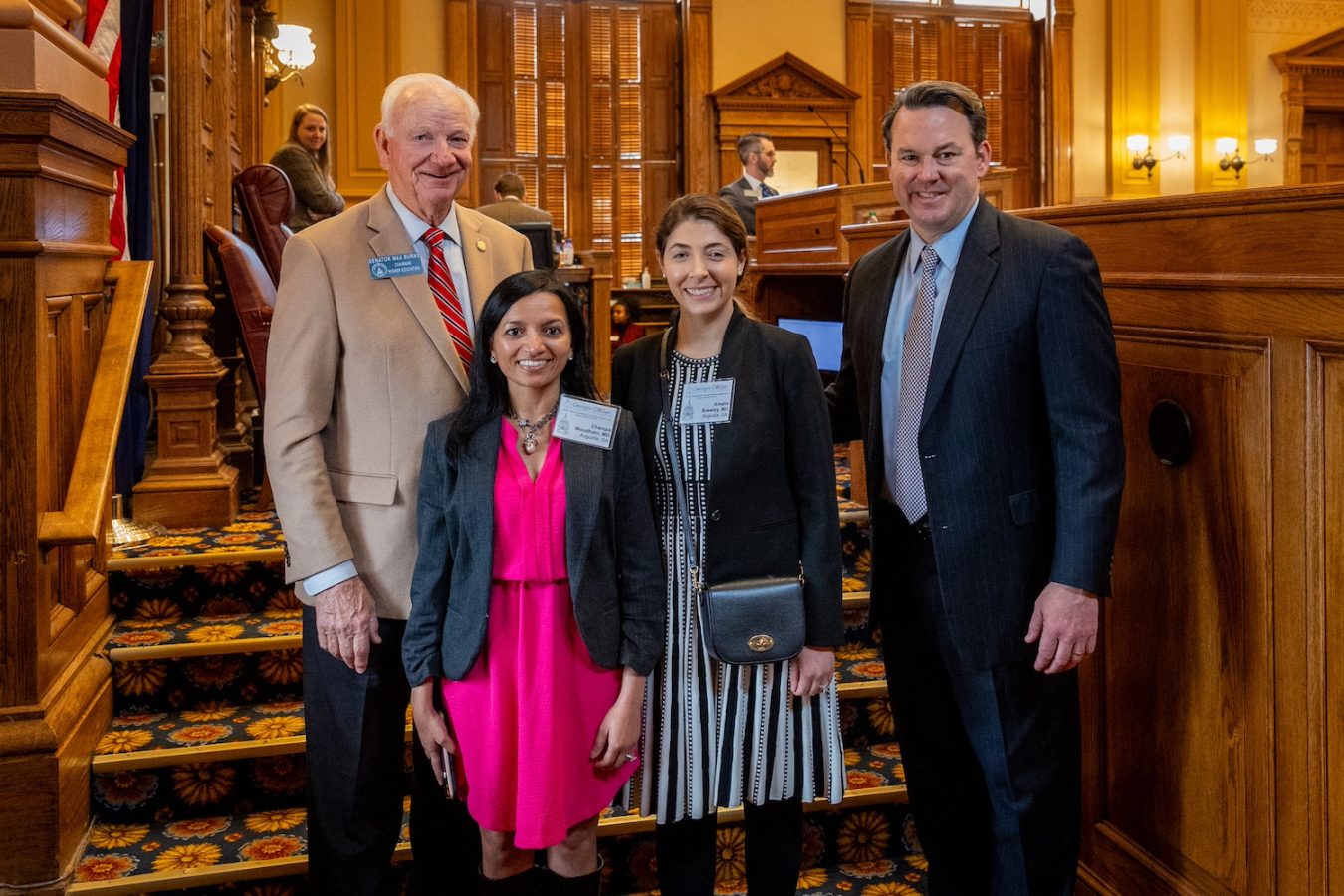 Four people stand in a large room in a government capitol building.