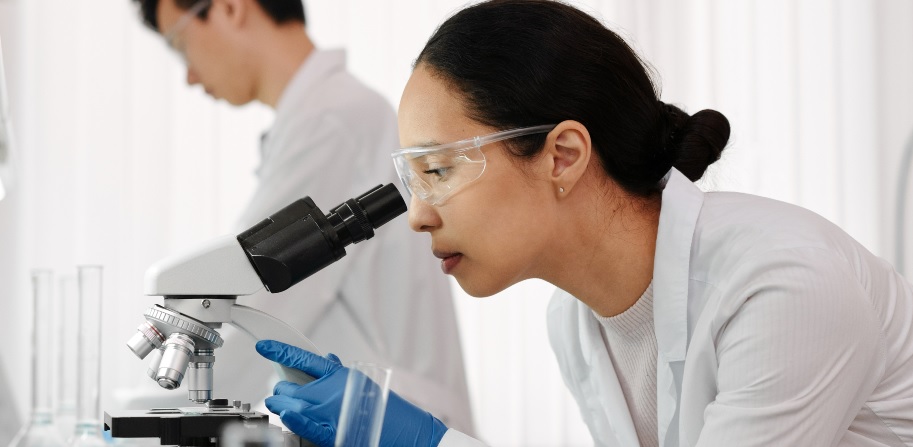 woman looks through microscope in lab