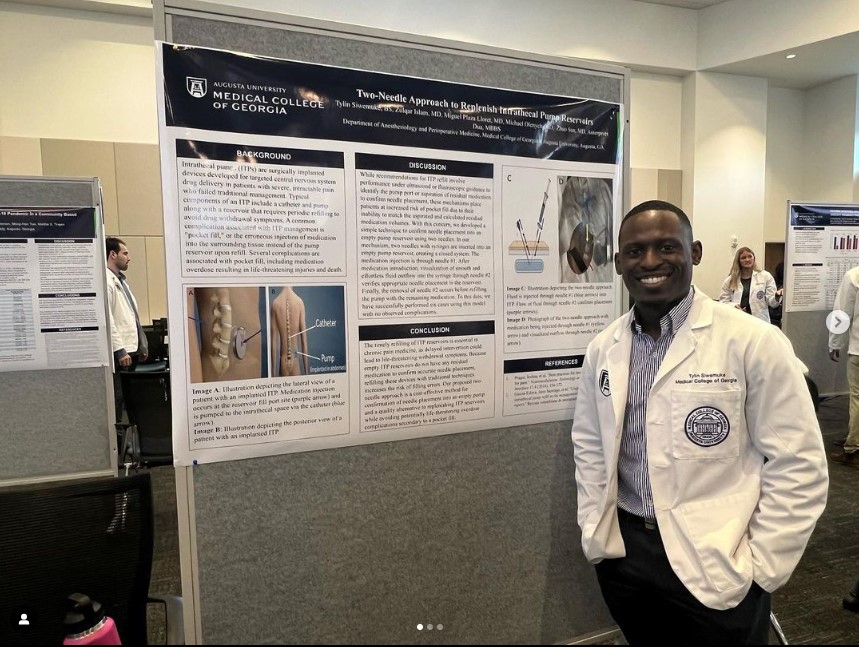 Student in white lab coat standing next to a poster of their work.