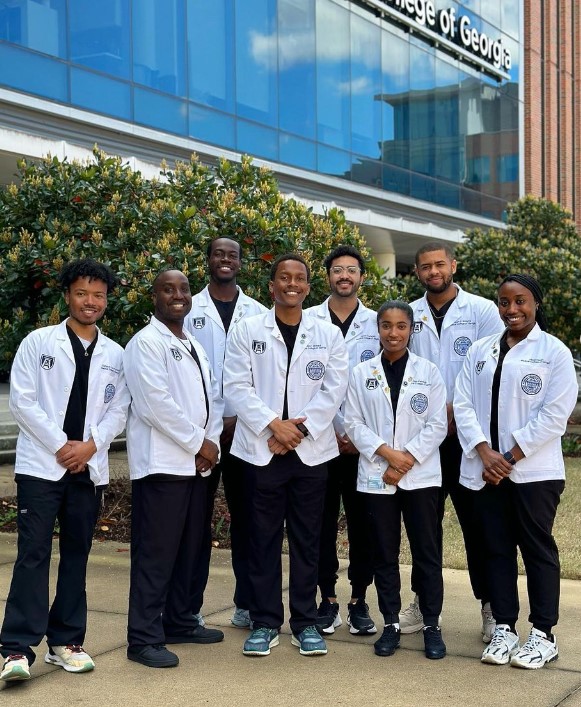 Photo of a group of students in lab coats in front of a building 