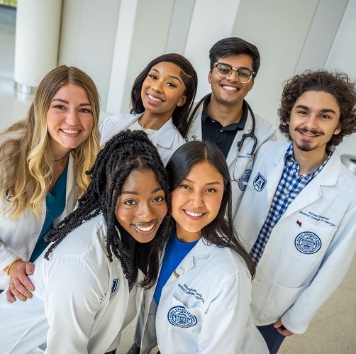 A group of MCG students in their white coats posing in the hallway of the hospital