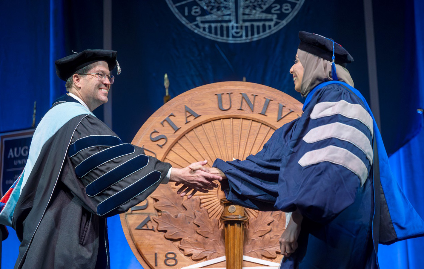 A man in a cap and gown shakes hands with a student in cap and gown