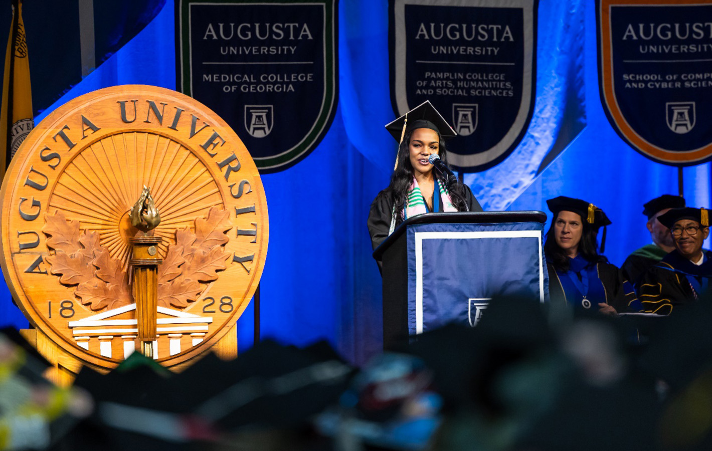 Female student in cap and gown speaking at podium