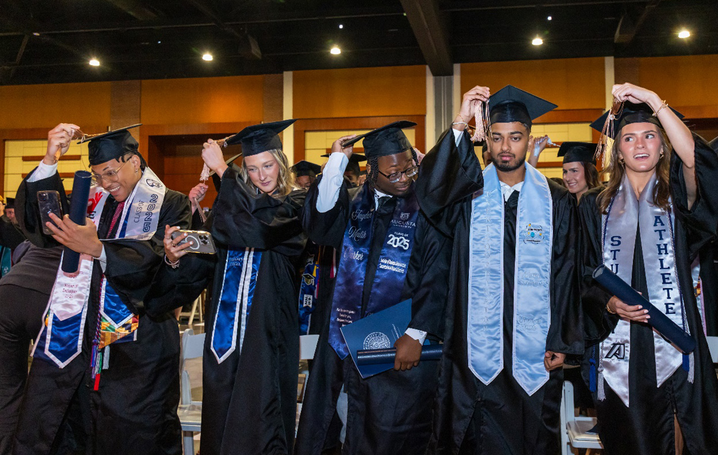 Group of five students in caps and gowns turning their tassels