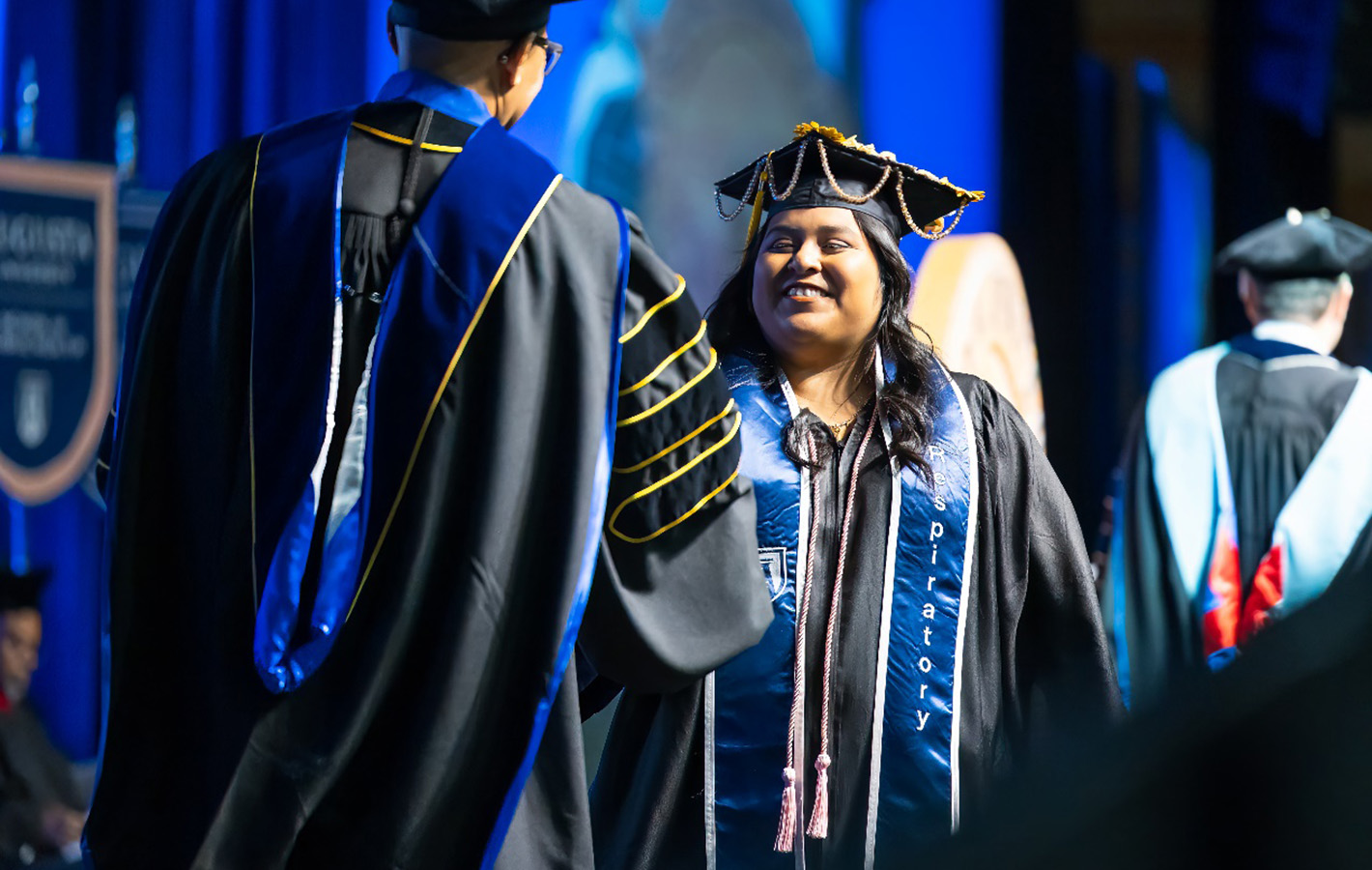 Female student shakes hands with professor in cap and gown