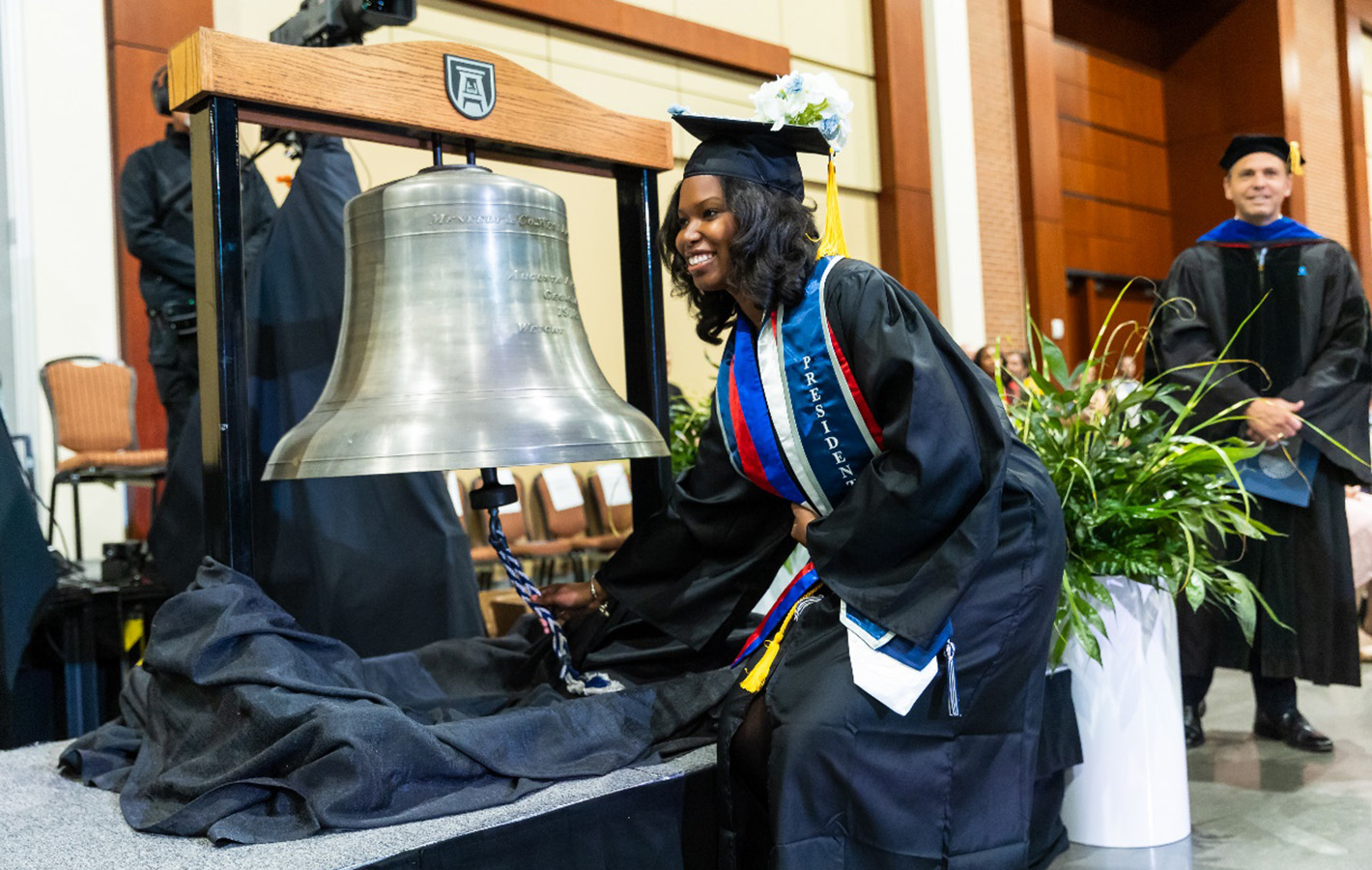 Female student in cap and gown squats next to bell