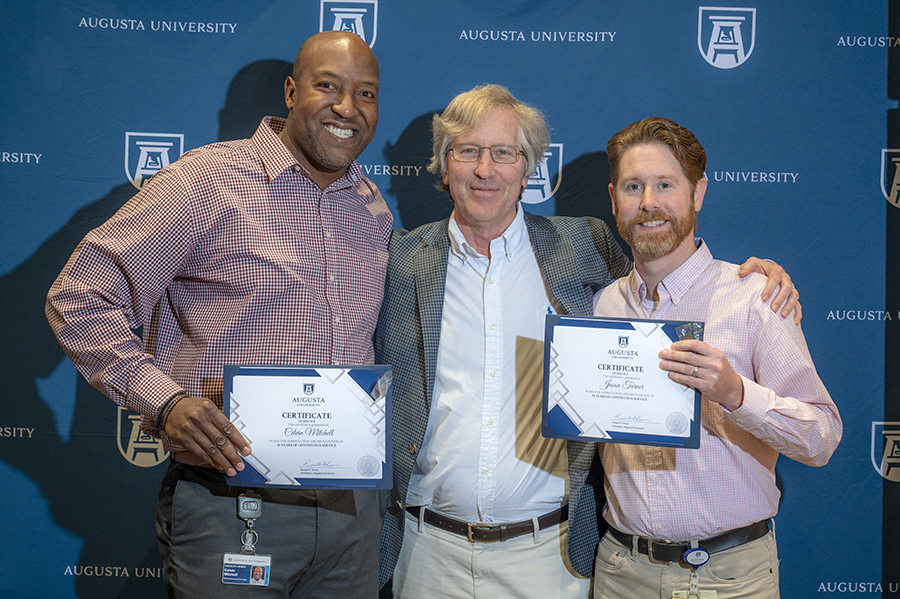 Three male employees posing for picture at ceremony