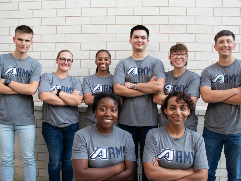 Cadets smile for a group photo in front of a white wall