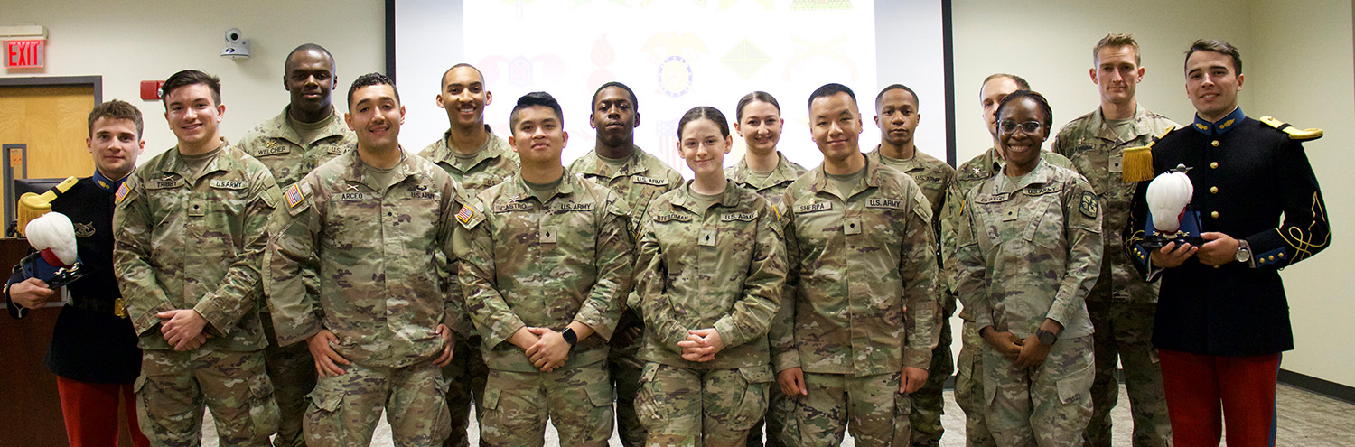 Cadets stand for photo in group in front of projector screen. Two French soldiers stand to the group’s sides.