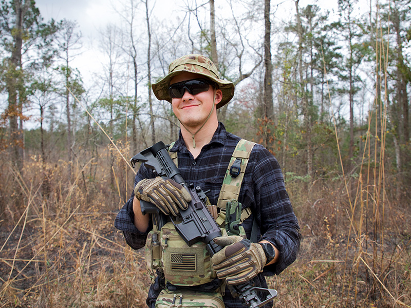 Cadet wearing black shirt and sunglasses crosses arms with M4 Slung across chest