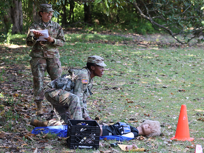 Cadet kneels over a mannequin looking across a field