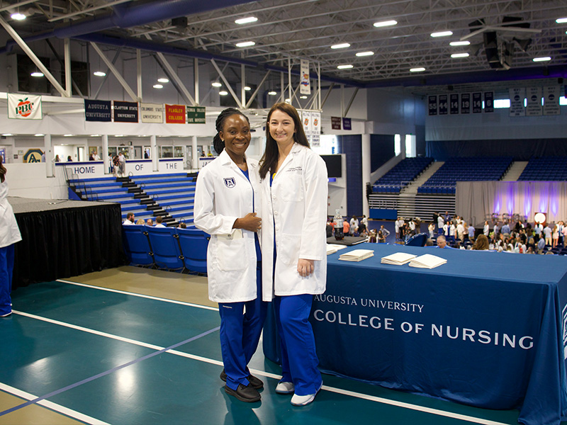 Two cadets wearing lab coats stand at the top of an arena for a ceremony