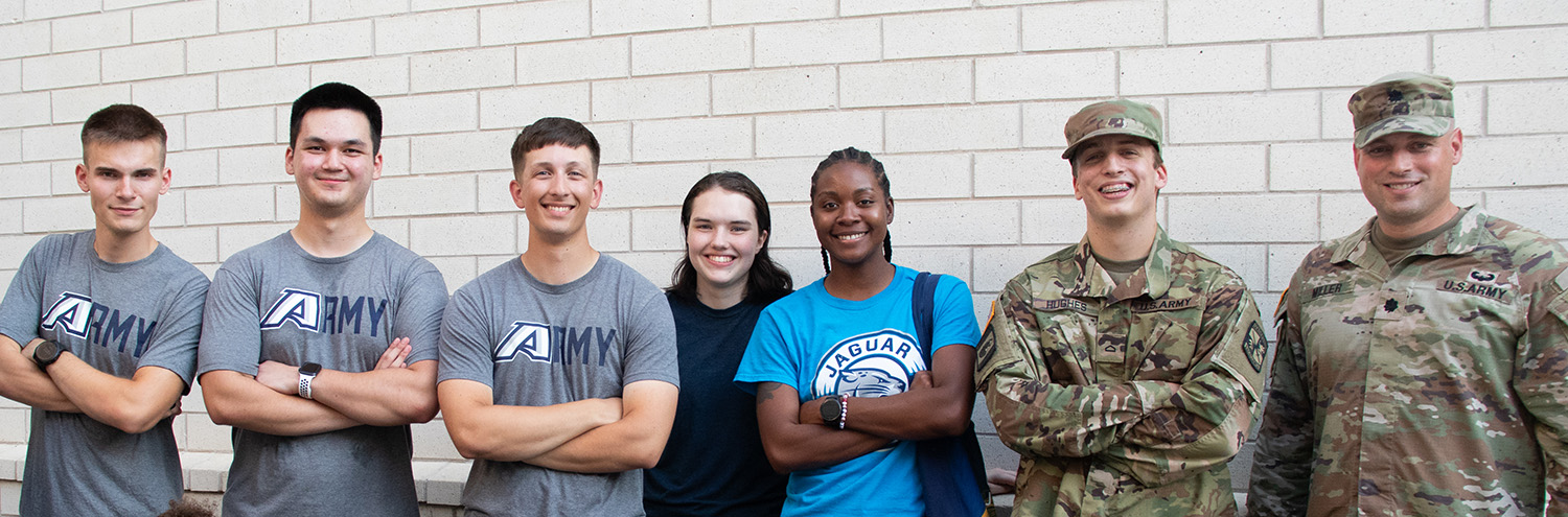 Cadets and guests stand and smile for photo in front of white wall