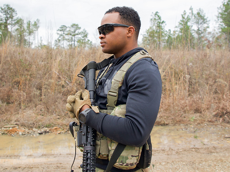 Cadet wearing black top and sunglasses crosses arms with M4 slung across chest