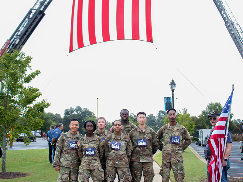 Cadets stand underneath flag hung up by firetrucks