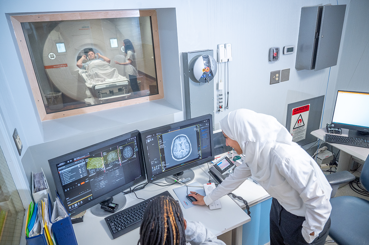 Neuro MRI Two students look over the controls to an MRI machine, while another student is inside the machine for a photo