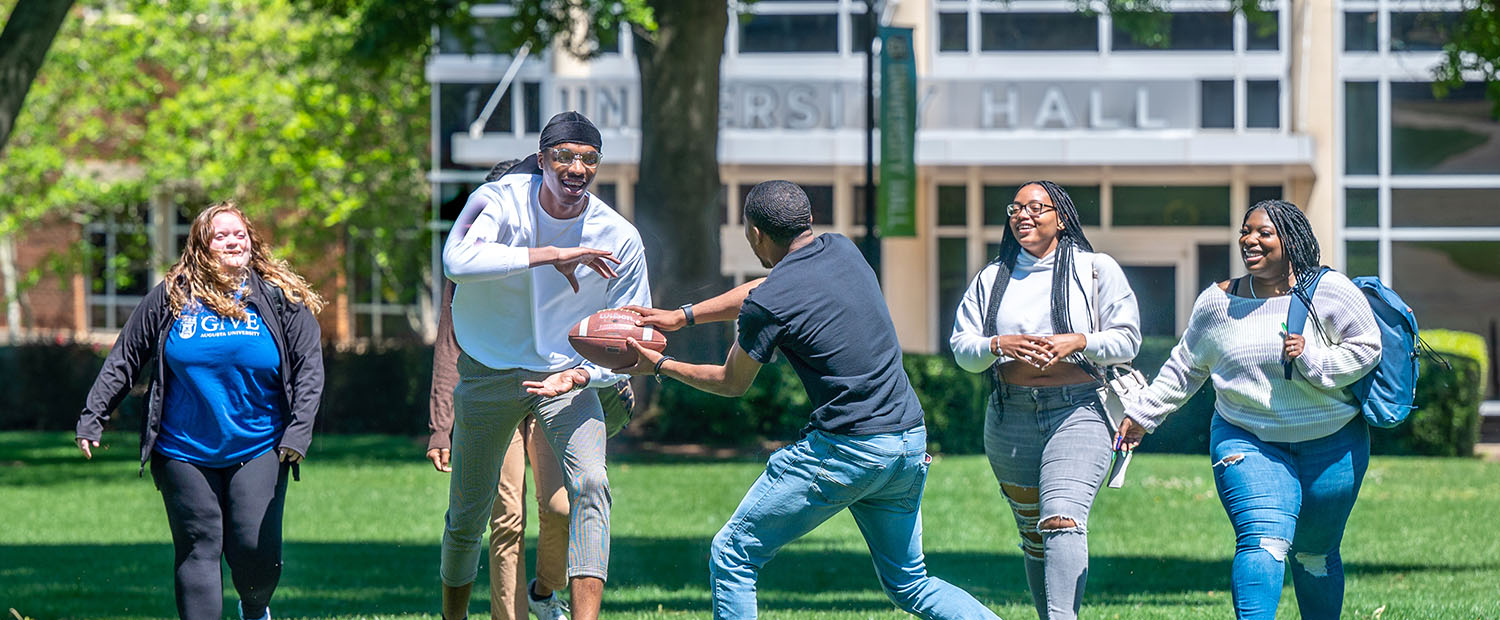 Male student handing off football to other male student while female students walk behind them