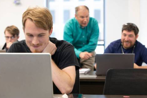 Professor advising students using laptops