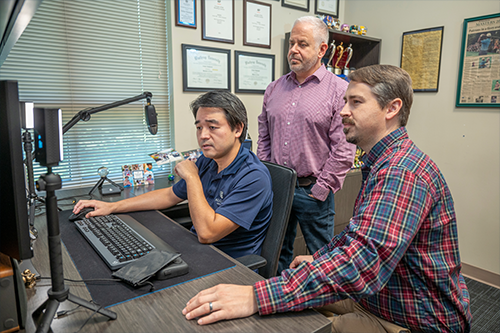 Three men gathered around a computer